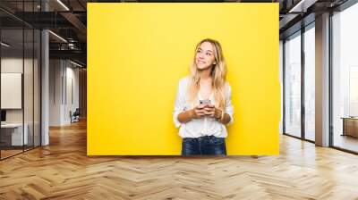 Portrait of a young woman using mobile phone isolated over yellow background Wall mural